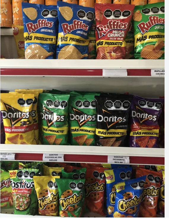Shelves of crisps and snack foods in a Mexican grocery store, every packet carrying black octagonal warning labels for excess calories, sugar, saturated fat and sodium